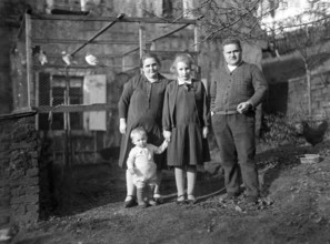 Family in front of a birdcage, 1930s, Family of four standing in a rural garden area, all looking