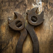 Two vintage adjustable wrenches lie side by side on a textured wooden surface, showing signs of