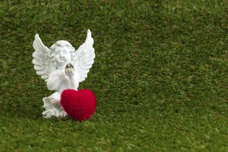 A white angel figure with a red heart on green grass