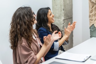 Two businesswomen clapping hands and smiling during a business meeting, showing appreciation and