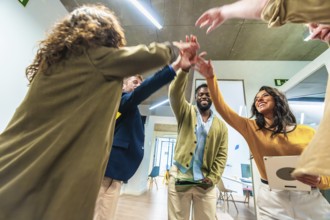 Coworkers joining hands, celebrating successful teamwork and cooperation in a modern office