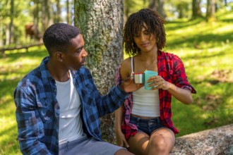Young couple taking a refreshing break during their hike, sharing drinks from reusable cups while