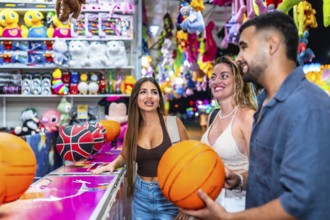Three friends having fun playing a basketball game at an amusement park, enjoying their summer