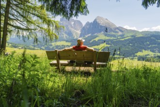 Person relaxing on a bench with a wide view of the mountains and green landscape, Alpe di Siusi,