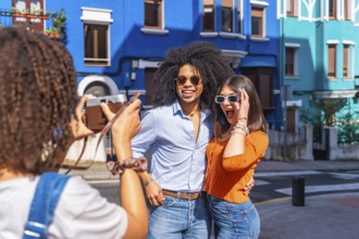 Young tourist taking a picture of her surprised friends posing in a colorful street during summer