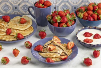 Chocolate syrup drips onto pancakes with strawberries, fresh strawberries in blue crockery in the