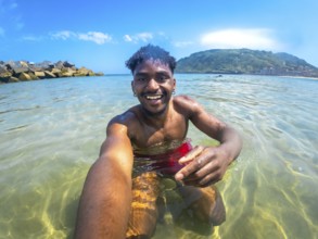 Young man enjoying a sunny summer day, capturing a joyful selfie while bathing in crystal clear sea
