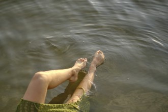 On a sunny day at the lake, a person enjoys the cool water, dipping her feet in while seated