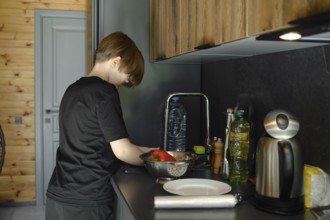 A boy washes vegetables in the sink and puts them in a colander, standing in profile at a sleek