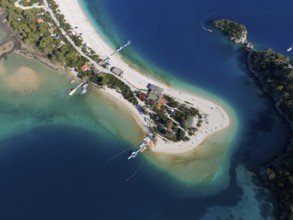 Aerial view of a small island with sandy beach and surrounding turquoise blue water and boats,