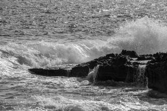 Rugged rocky coast and foaming spray, on Stecci beach, black and white photograph, near Capoliveri,