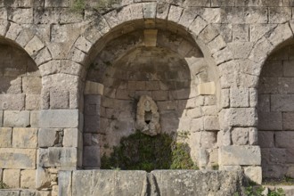Ancient round arches with a sculpture and moss growth, arcade, lower terrace, Pan, Asklipion,