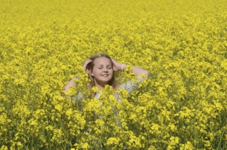 Blonde girl, 15 years old, stands smilingly in flowering rapeseed field in Ystad Municipality,