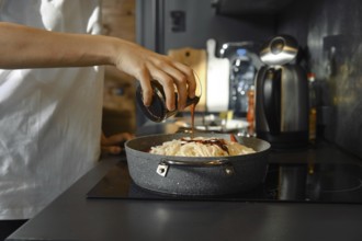 Unrecognizable person adds a soy sauce to a skillet filled with fresh vegetables and noodles on the