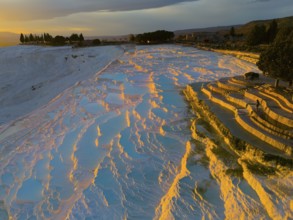 Landscape with terraces and water that glows orange and blue in the sunset light, aerial view,