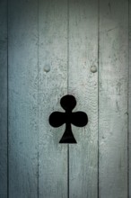 A black club symbol is prominently displayed on a weathered blue wooden door. The door's texture