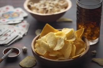 Chips, popcorn and a drink next to playing cards and a cigarette
