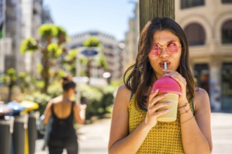 Fashionable young woman sipping a cold beverage through a straw, enjoying a sunny day in the city