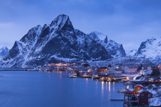 Fishermen's Village in front of snowy mountain range at the coastline in winter, Lofoten, Norway