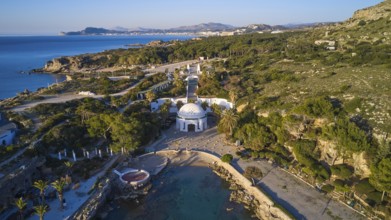 Drone shot, morning light, aerial view with domed building in green coastal landscape on the blue