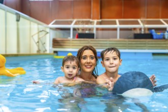 Happy mother enjoying time in the swimming pool with her sons, playing joyfully with colorful