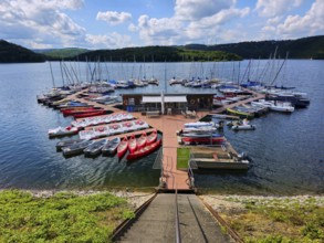 A colourful little marina with boats, sailing boats and pedal boats docked at a jetty on a lake,