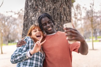 Two happy young students are making the victory sign while taking a selfie with a smartphone in a