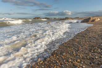 The waves crash gently against a rocky shoreline at sunset, creating a tranquil atmosphere. The