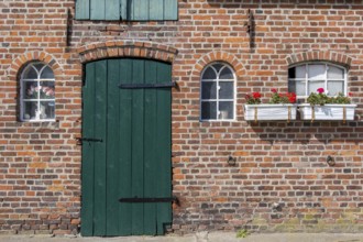 Nostalgic brick wall with green door and white windows, decorated with flower pots, Föhr,