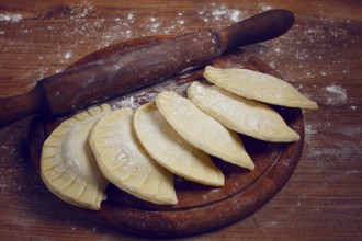Raw chebureks, mini, on a cutting board, wooden table, close-up, no people