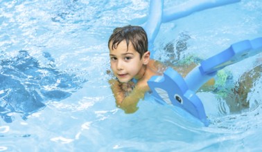 Happy boy enjoying playtime with an inflatable toy whale in a sparkling swimming pool, soaking up
