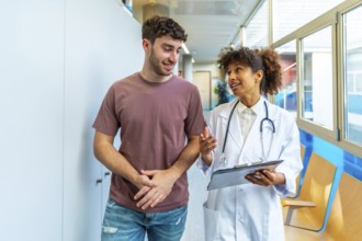 Doctor holding clipboard and explaining diagnosis to patient while walking in hospital corridor