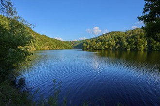 Peaceful lake surrounded by green hills under a clear sky, slight reflection in the water, summer,
