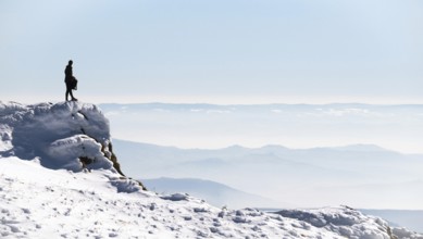 Standing on a rocky ledge, a walker takes in the breathtaking view of snow-covered mountains in