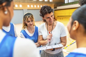 Smiling female coach explaining basketball game strategy to her team using a clipboard in a gym