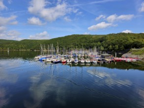 Quiet harbour with sailing boats under a blue sky and reflections in the water, surrounded by