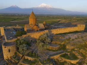 Historical monastery against a mountain backdrop in daylight surrounded by stone walls, aerial