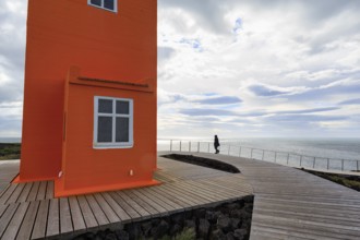 Orange lighthouse Skálasnagaviti or Svörtuloft with wooden plank path, walker, Skalasnagi,