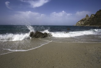Waves crashing against rocks on the beach, blue sky in the background, Ricadi, Capo Vaticano