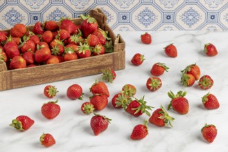 Strawberries scattered on a marble slab, next to a box full of strawberries