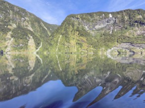 Mountains with reflections in the water against a blue sky in Doubtful Sound, South Island, New
