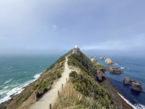 Nugget Point Lighthouse with Nugget Rocks in front of a blue sky, South Island, New Zealand,