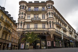 Historic building with palm trees and shop windows in an urban environment under a cloudy sky,