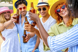 Group of cheerful multiracial young people wearing summer clothes and hats toasting and drinking