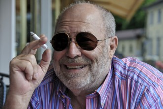 Portrait of a smiling elderly gentleman with a beard, sunglasses and a cigarette in his hand,