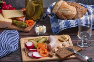 Rustic arrangement with sausage, cheese, vegetables, mustard and bread on a laid table