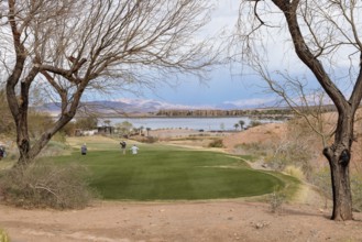 Threesome of senior golfers teeing off while playing on a golf course along the shoreline of Las