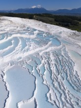 Cascading terraces of turquoise water and white limestone in the foreground, mountains in the