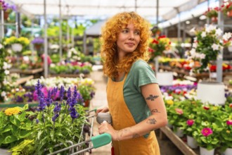 Young woman pushing a shopping cart while selecting vibrant flowers in a garden center greenhouse,