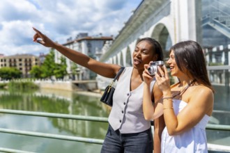 Two female tourists capturing photos and enjoying the vibrant cityscape by the river during a sunny